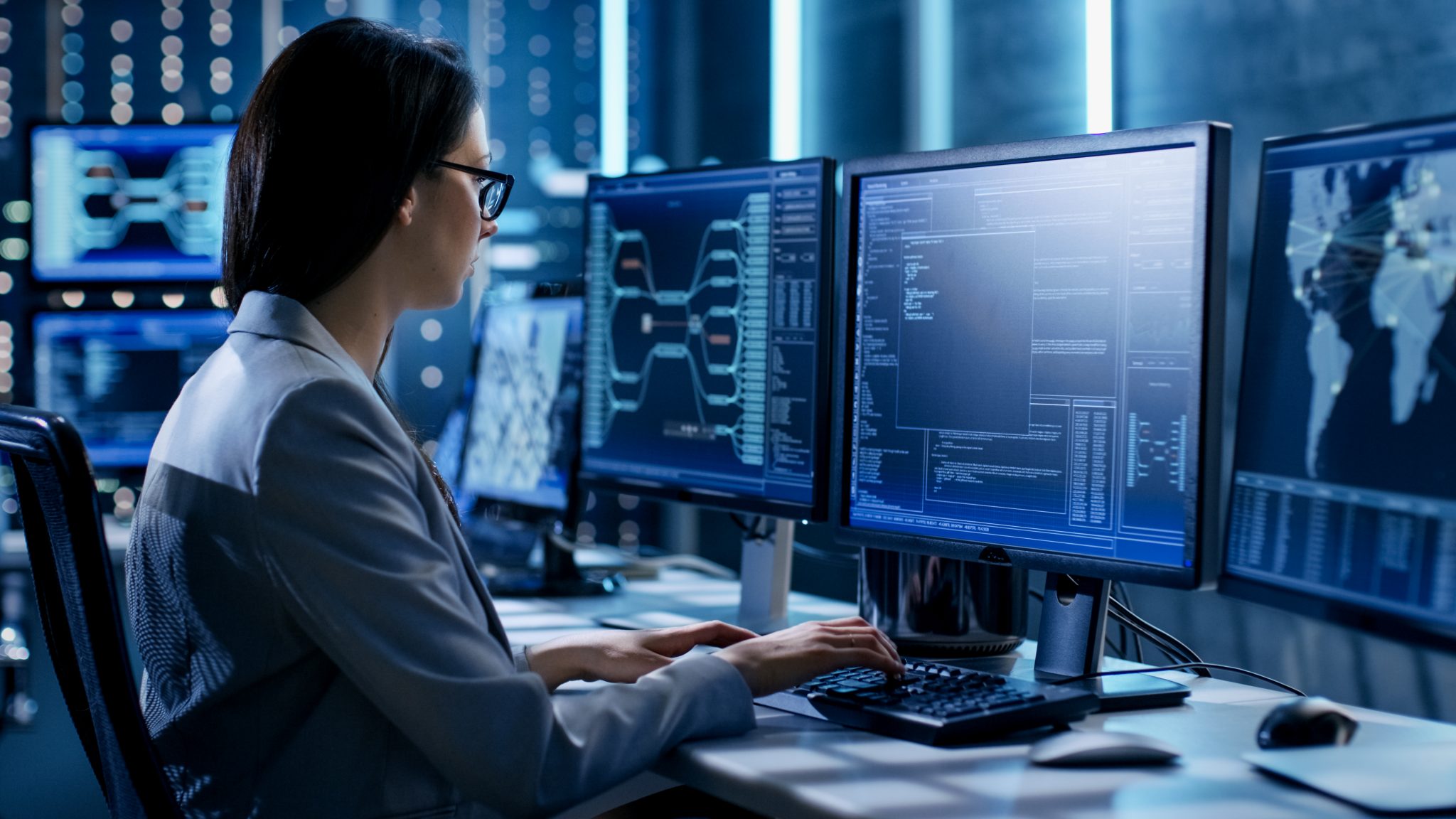 Female System Engineer Controls Operational Proceedings. In the Background Working Monitors Show Various Information.